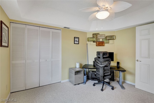 office area with ceiling fan, a tray ceiling, and light carpet