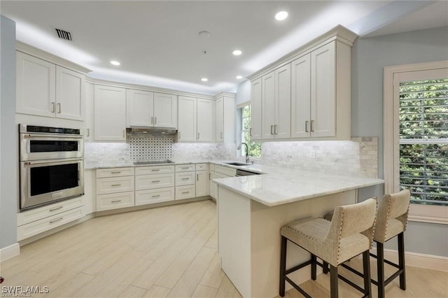 kitchen featuring white cabinetry, sink, stainless steel double oven, kitchen peninsula, and a breakfast bar area