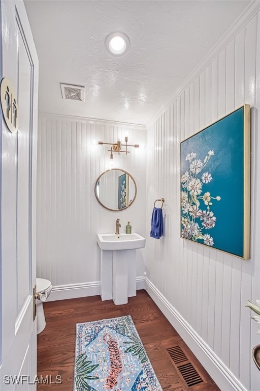 bathroom featuring wood-type flooring, ornamental molding, toilet, and wood walls