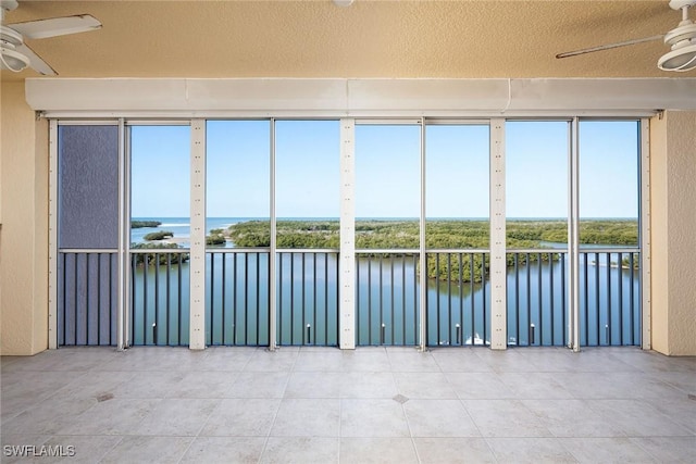 unfurnished sunroom featuring ceiling fan, a wealth of natural light, and a water view