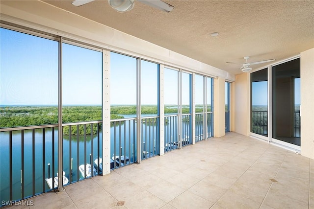 unfurnished sunroom featuring ceiling fan and a water view