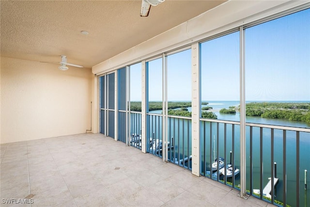 unfurnished sunroom with ceiling fan and a water view