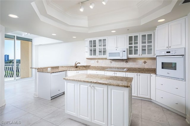 kitchen featuring white appliances, a tray ceiling, white cabinetry, and a kitchen island