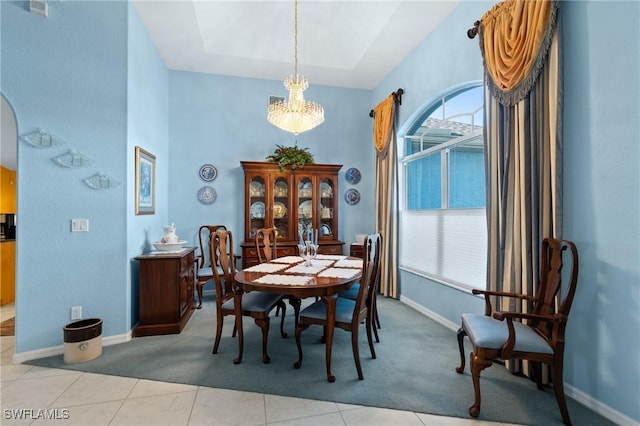 dining space with a raised ceiling, light tile patterned flooring, and a notable chandelier