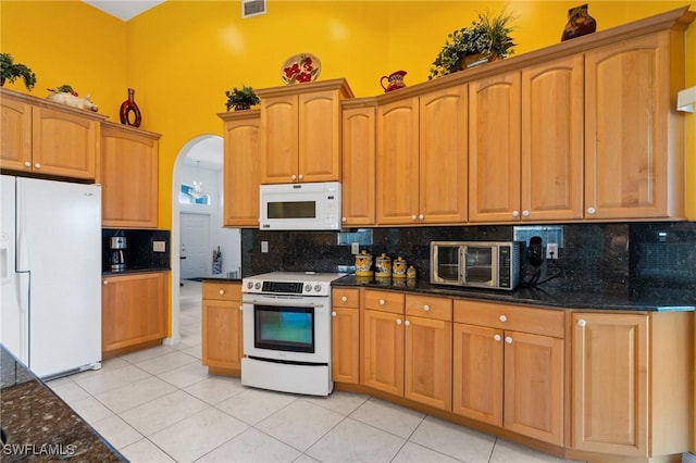 kitchen with dark stone countertops, light tile patterned floors, white appliances, and decorative backsplash