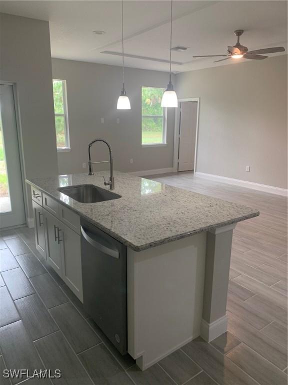 kitchen featuring a wealth of natural light, wood finish floors, a kitchen island with sink, a sink, and stainless steel dishwasher