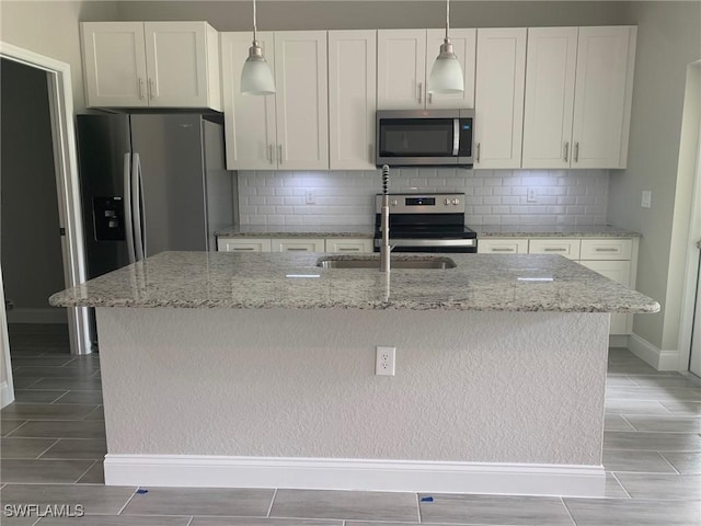 kitchen featuring stainless steel appliances, backsplash, a kitchen island with sink, and white cabinetry