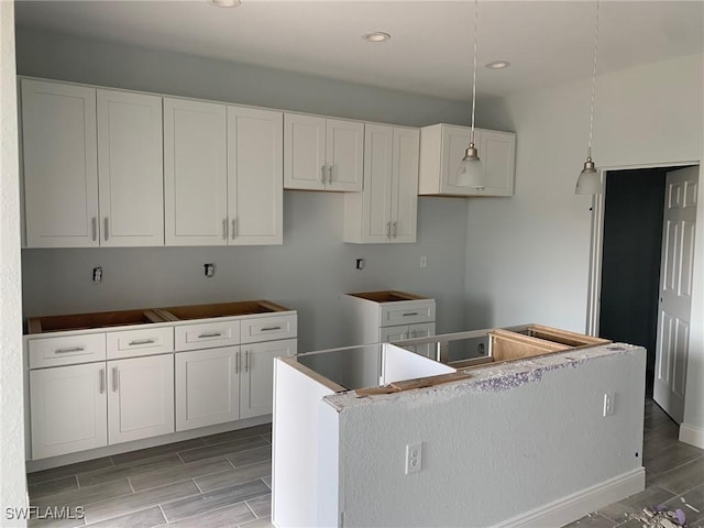 kitchen with wood finish floors, a kitchen island, pendant lighting, and white cabinets