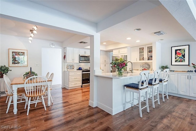 kitchen with white cabinets, appliances with stainless steel finishes, dark hardwood / wood-style flooring, kitchen peninsula, and a breakfast bar