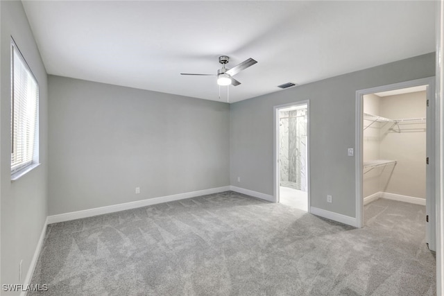 unfurnished bedroom featuring a walk in closet, light carpet, a closet, and ceiling fan