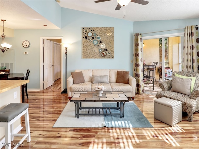 living room with lofted ceiling, light wood-type flooring, and ceiling fan with notable chandelier