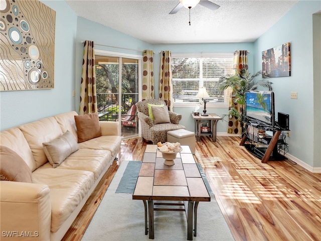 living room featuring light wood-type flooring, ceiling fan, and a textured ceiling