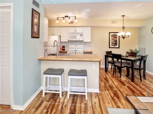 kitchen with pendant lighting, white appliances, white cabinets, tasteful backsplash, and kitchen peninsula