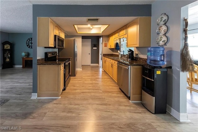 kitchen with light brown cabinetry, a raised ceiling, sink, stainless steel appliances, and light hardwood / wood-style flooring