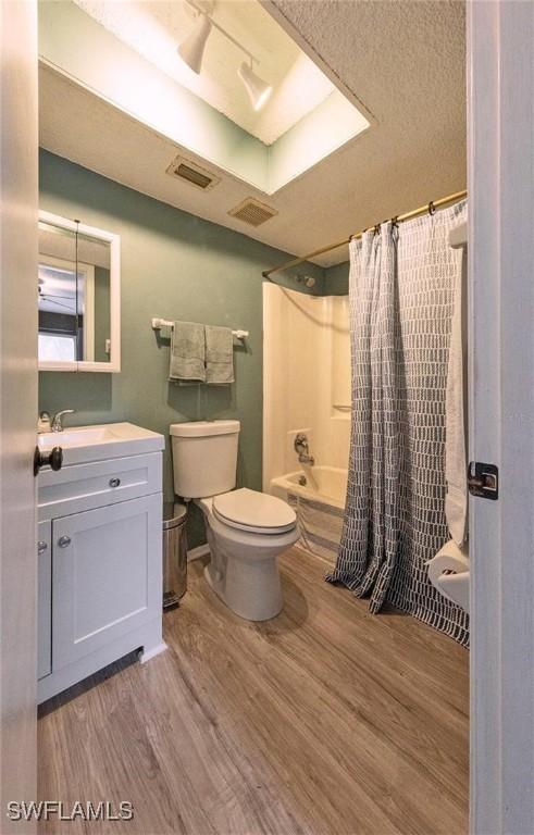 full bathroom with hardwood / wood-style flooring, vanity, shower / bath combination with curtain, and toilet