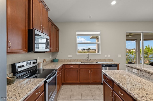 kitchen featuring brown cabinetry, appliances with stainless steel finishes, light stone countertops, a sink, and light tile patterned flooring