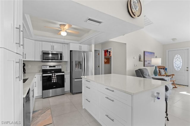 kitchen featuring stainless steel appliances, a raised ceiling, light tile patterned floors, white cabinets, and a center island