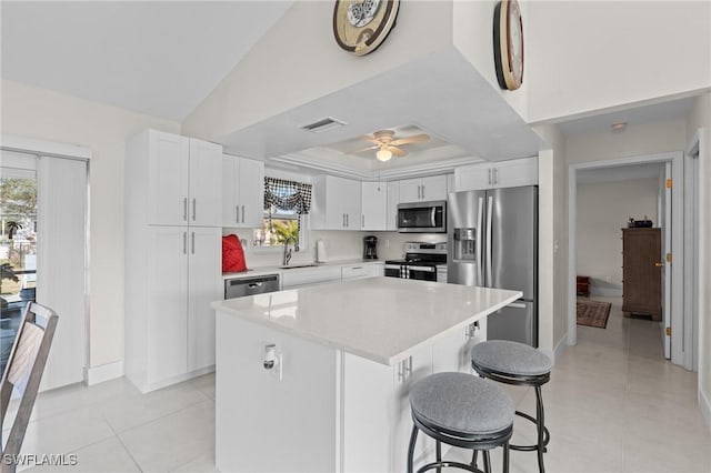 kitchen featuring ceiling fan, white cabinetry, a kitchen breakfast bar, a kitchen island, and appliances with stainless steel finishes