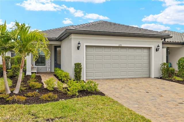 ranch-style house with a tiled roof, decorative driveway, an attached garage, and stucco siding