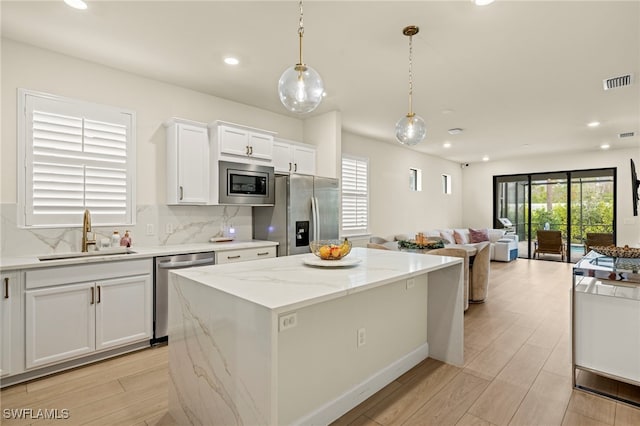 kitchen featuring a kitchen island, appliances with stainless steel finishes, open floor plan, pendant lighting, and a sink