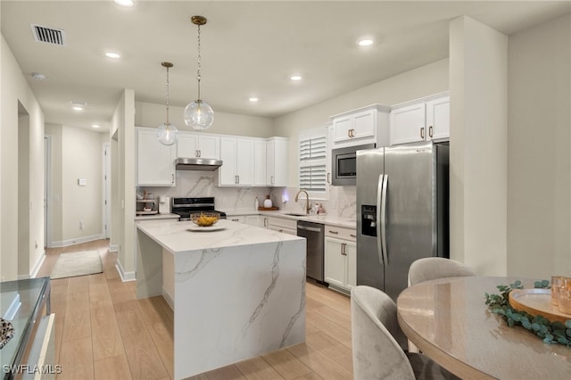 kitchen with stainless steel appliances, a kitchen island, visible vents, white cabinets, and decorative light fixtures