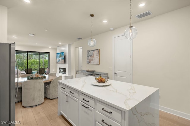 kitchen featuring visible vents, freestanding refrigerator, decorative light fixtures, a center island, and white cabinetry