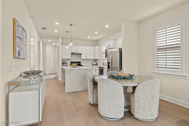 kitchen with appliances with stainless steel finishes, a center island, light countertops, white cabinetry, and pendant lighting