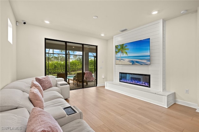 living room featuring recessed lighting, visible vents, light wood-style flooring, a glass covered fireplace, and baseboards