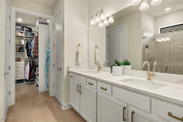 bathroom with a walk in closet, a sink, a shower stall, and wood finished floors