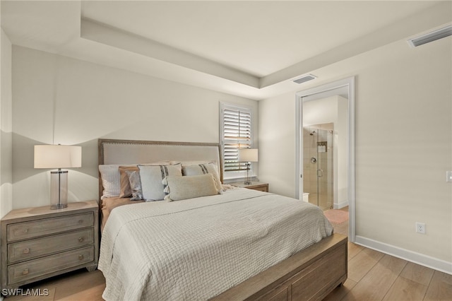 bedroom with baseboards, visible vents, connected bathroom, and light wood finished floors