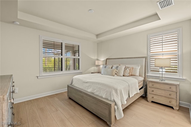 bedroom with light wood finished floors and a tray ceiling