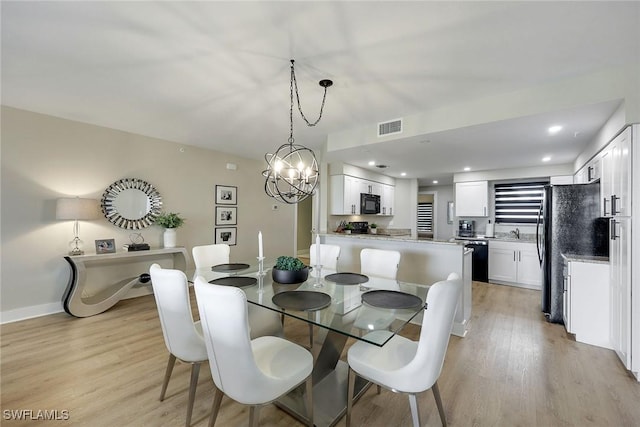 dining room with light wood-type flooring, an inviting chandelier, and sink