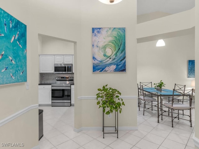 kitchen featuring appliances with stainless steel finishes, light tile patterned floors, white cabinets, and backsplash