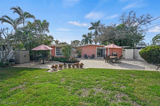 rear view of property featuring a patio area, a lawn, and a storage shed