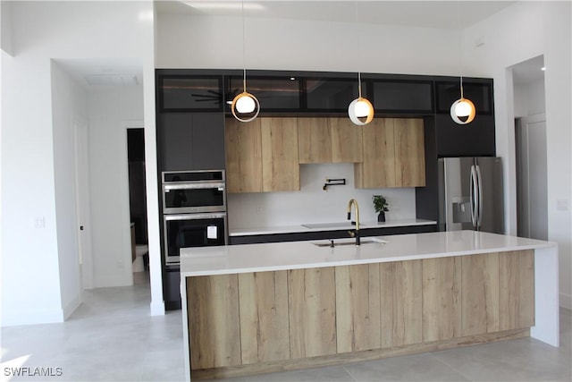 kitchen featuring sink, appliances with stainless steel finishes, pendant lighting, and a kitchen island with sink