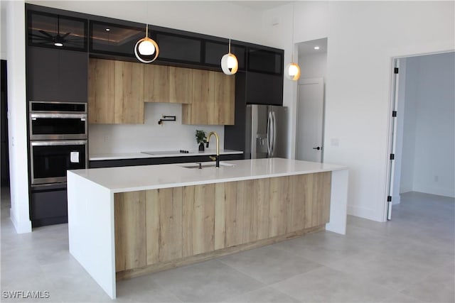 kitchen with stainless steel appliances, a center island with sink, hanging light fixtures, and sink