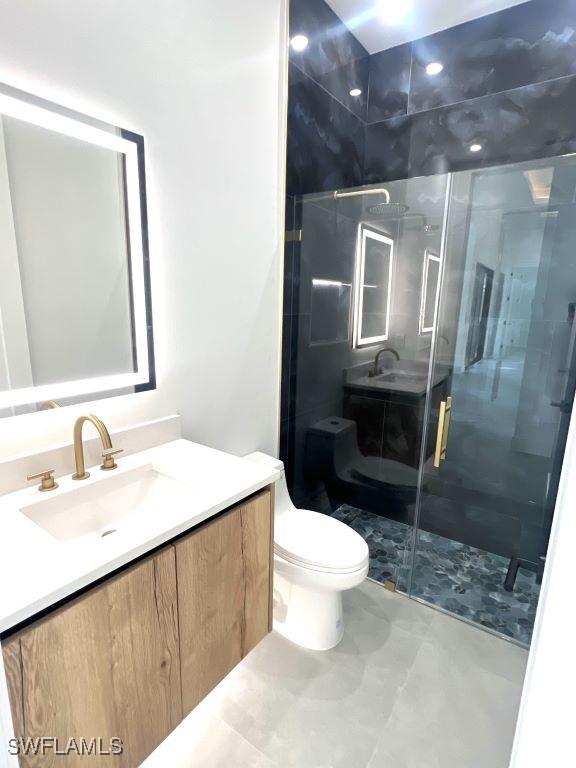 bathroom featuring toilet, vanity, and a shower with door