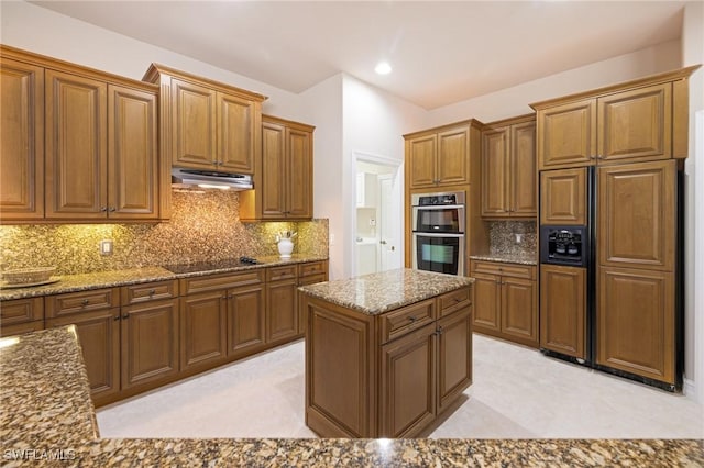 9284 Trieste Dr, Fort Myers, FL 33913 - kitchen featuring decorative backsplash, under cabinet range hood, stone countertops, black electric stovetop, and double oven