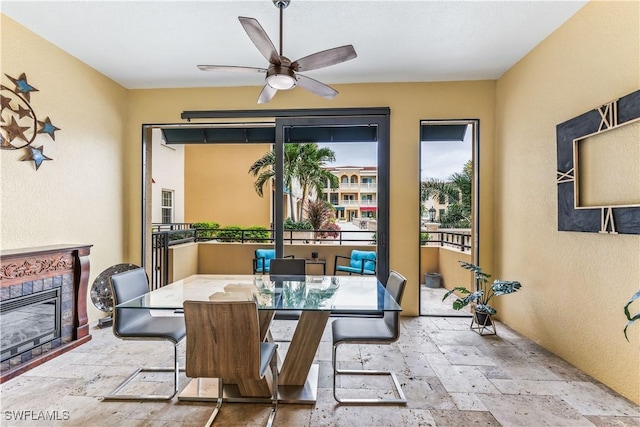 dining space with a tiled fireplace and ceiling fan