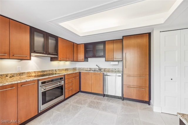 kitchen with appliances with stainless steel finishes, glass insert cabinets, a sink, and light stone counters