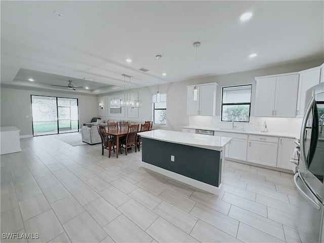 kitchen with white cabinets, a center island, hanging light fixtures, a raised ceiling, and ceiling fan