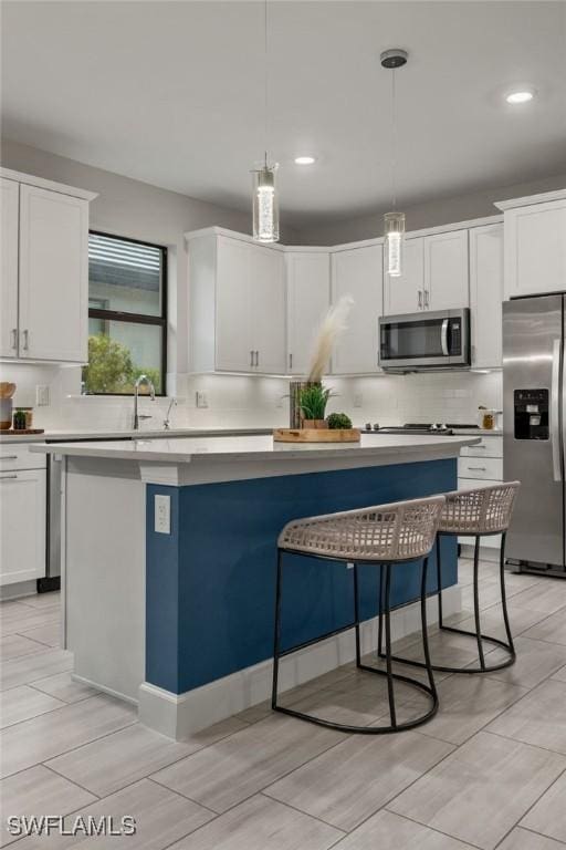 kitchen with white cabinets, stainless steel appliances, a center island, and hanging light fixtures