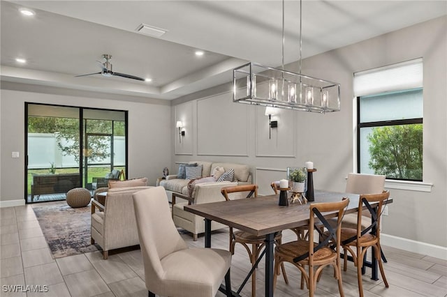 dining space with plenty of natural light, ceiling fan with notable chandelier, and a tray ceiling