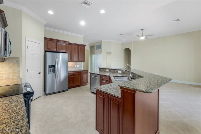 kitchen featuring tasteful backsplash, ceiling fan, a center island with sink, sink, and appliances with stainless steel finishes