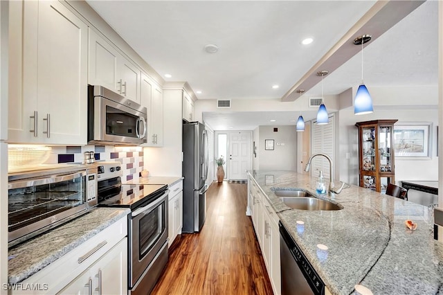 kitchen with appliances with stainless steel finishes, light stone counters, sink, white cabinetry, and hanging light fixtures