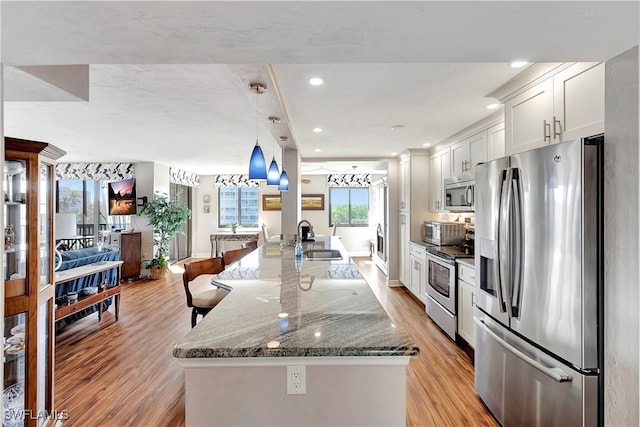 kitchen with appliances with stainless steel finishes, light wood-type flooring, sink, pendant lighting, and white cabinetry