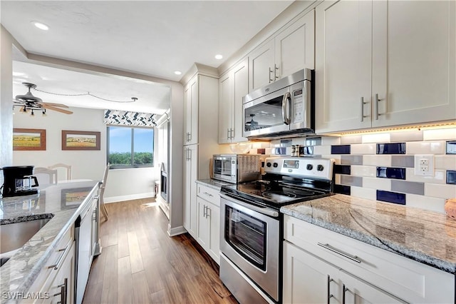 kitchen featuring light wood-type flooring, tasteful backsplash, light stone counters, white cabinetry, and stainless steel appliances