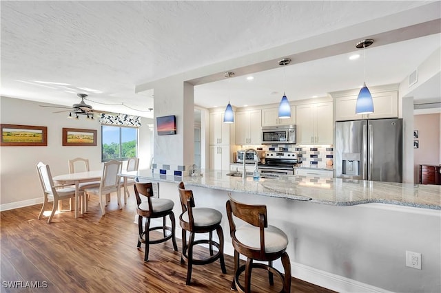 kitchen featuring tasteful backsplash, light stone counters, stainless steel appliances, pendant lighting, and white cabinets