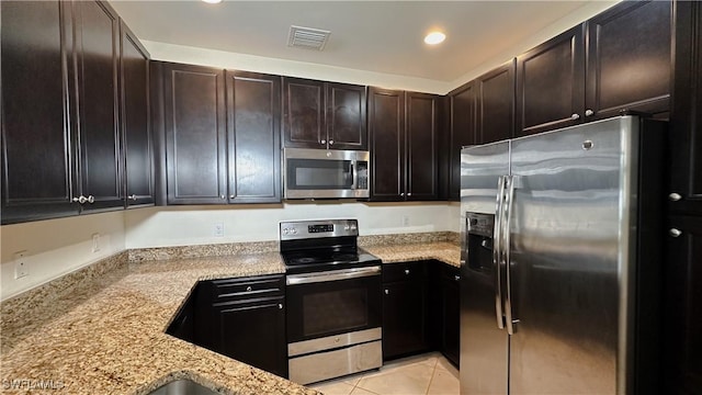 kitchen with light tile patterned floors, dark brown cabinets, light stone counters, and stainless steel appliances