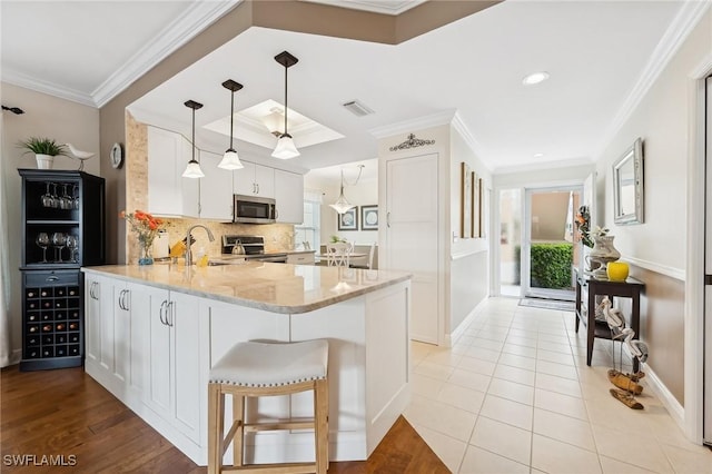 kitchen with appliances with stainless steel finishes, kitchen peninsula, ornamental molding, white cabinets, and decorative light fixtures